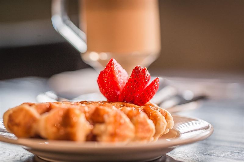 A waffle with strawberries and a latte