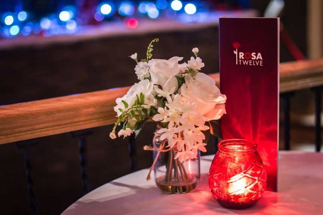 A Rosa Twelve menu with flowers and a candle set at a table for two